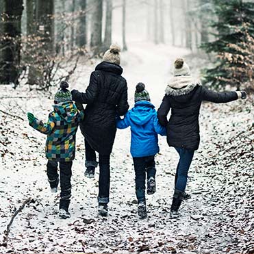 Family skipping down a snow covered path in the forest.