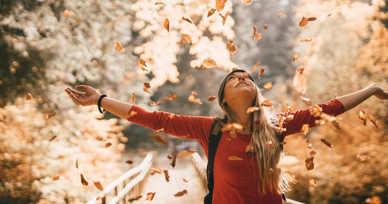 Woman with open arms watching leaves fall
